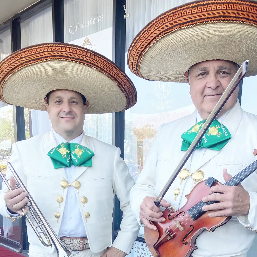 Dos músicos del mariachi con traje blanco y moño verde, uno con la trompeta y otro con el violín