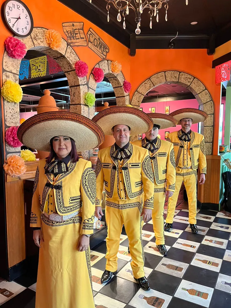 Cuatro integrantes del mariachi con traje amarillo bordado y sombrero en un restaurante decorado