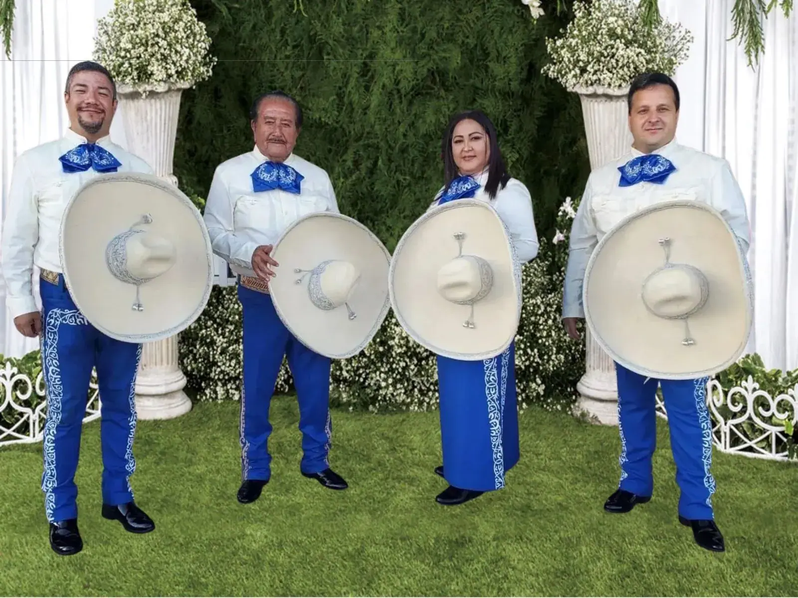 Mariachi America Canta con trajes de charro blancos y azules en un escenario con flores