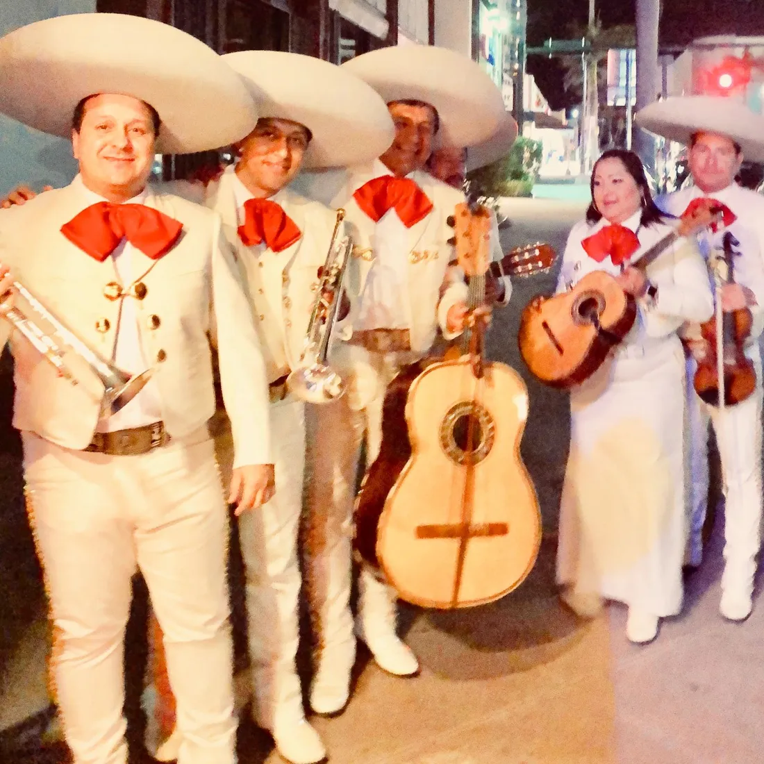 Mariachi con trajes de charro blancos y moños rojos listo para tocar en una boda de noche