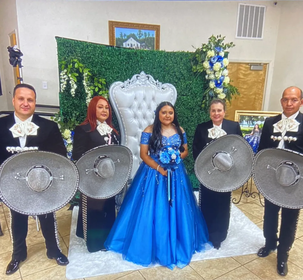 Quinceañera de vestido azul con cuatro integrantes del mariachi de charro negro y sombreros plateados